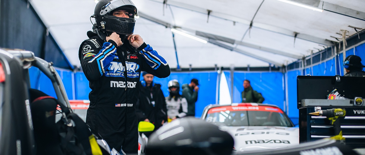 Mazda Racer Adjusting Helmet Next to Vehicle